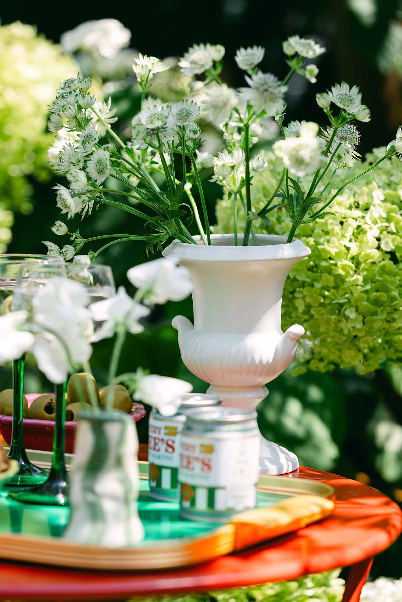 Vintage ceramic planter on garden table surrounded by plants, bowl of olives and cocktails