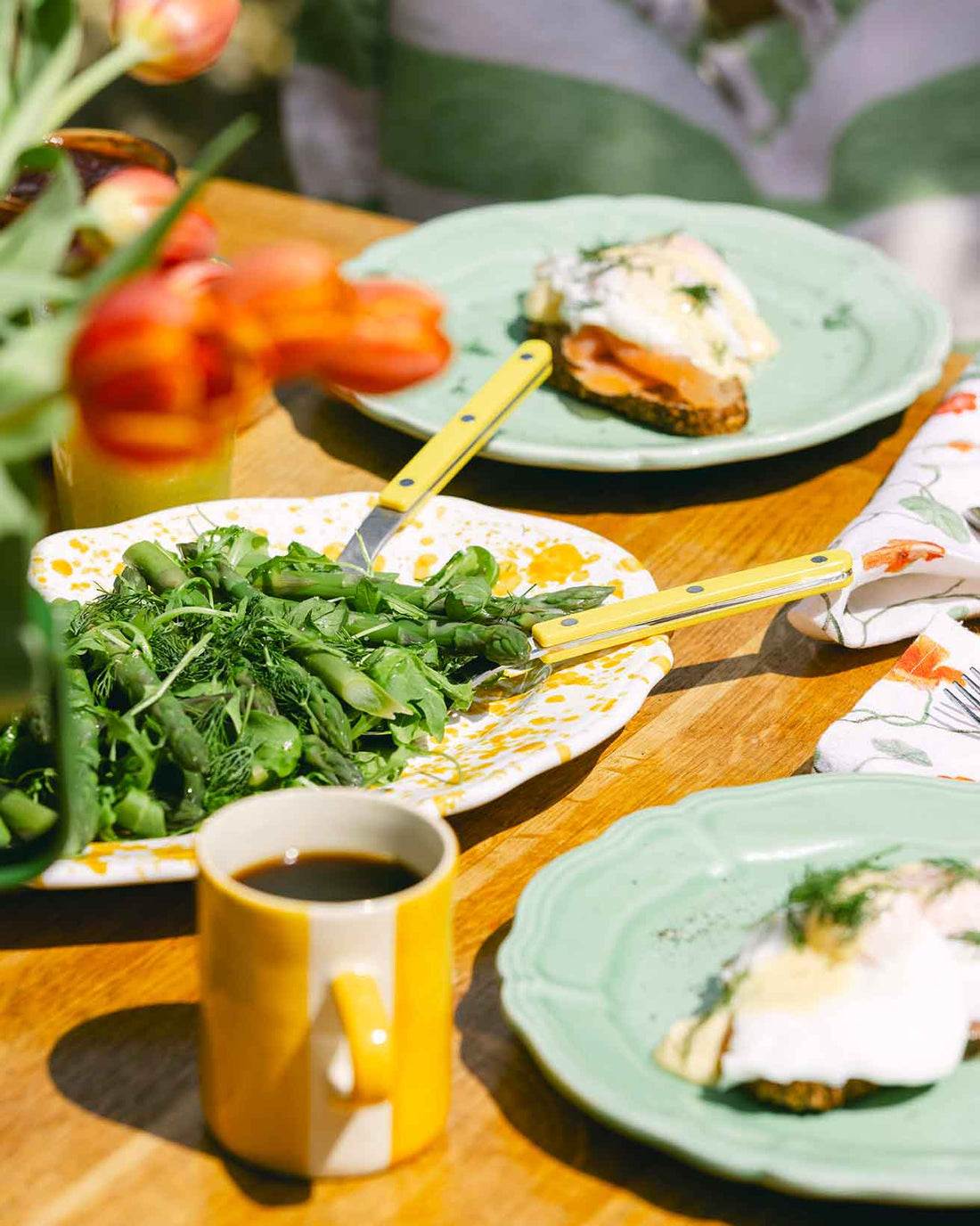 Outdoor dining table with mug, plates, salad servers and a vase of tulips. LAMP LDN LIVING