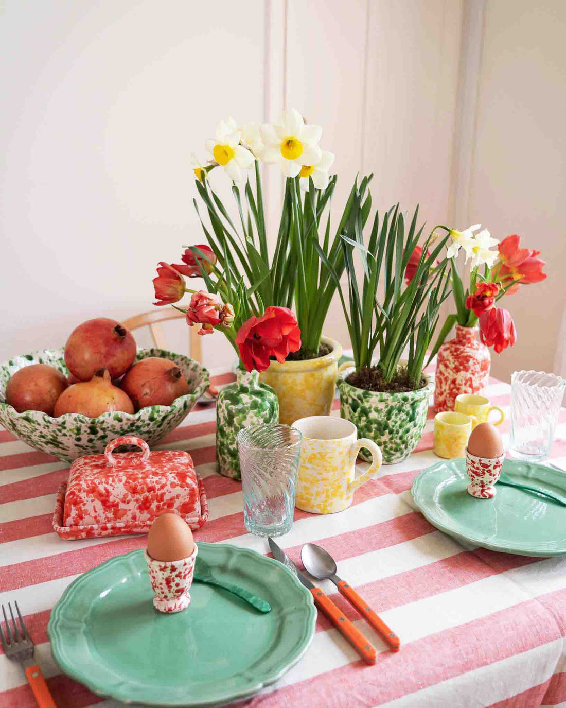 Dining table set with decor including plates, eggs, and flowers on a striped tablecloth. LAMP LDN LIVING