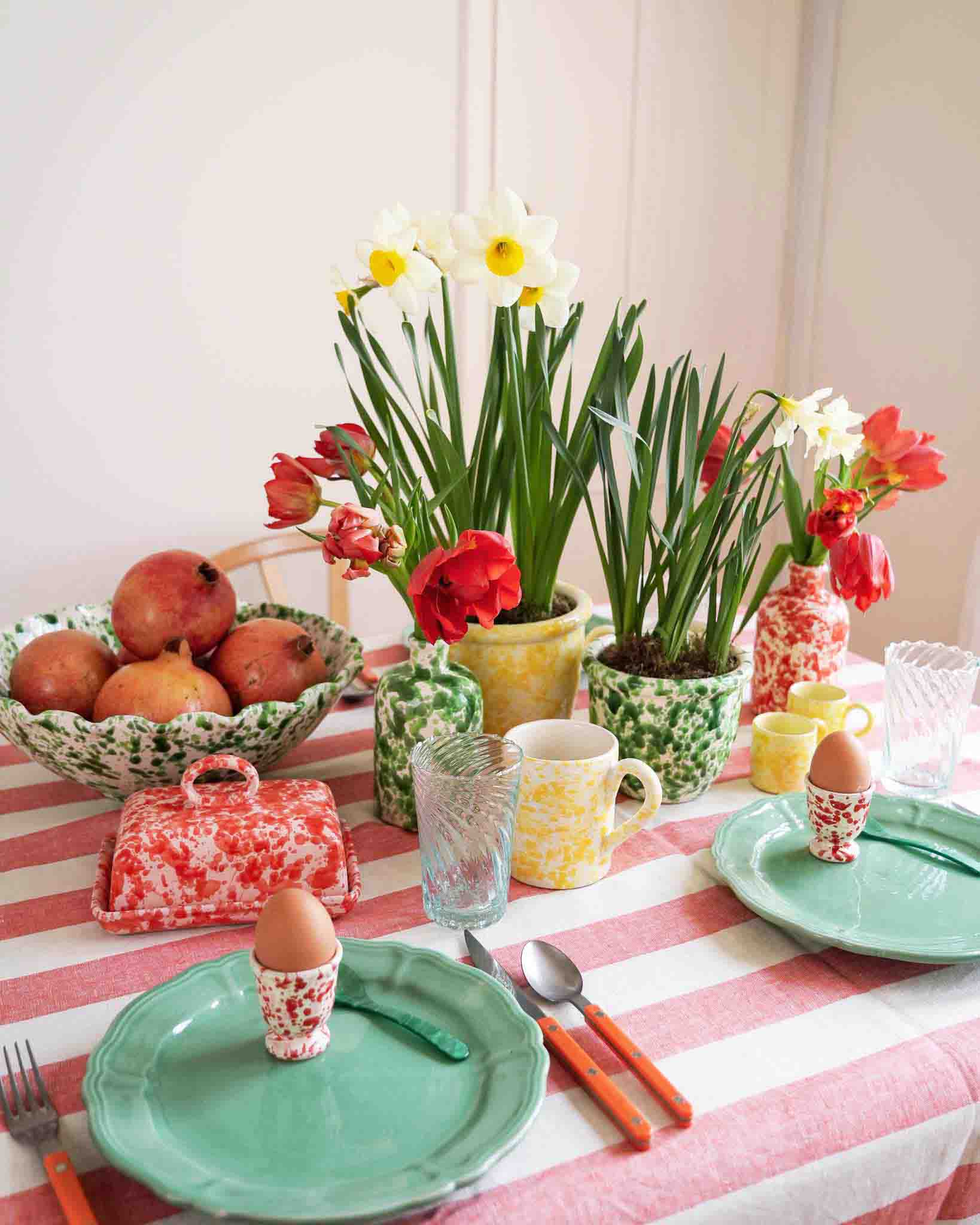 Dining table set with decor including plates, eggs, and flowers on a striped tablecloth. LAMP LDN LIVING