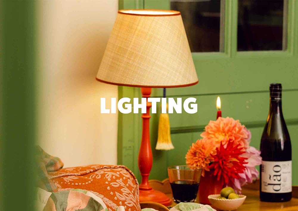 Living room with a lamp, wine bottle, and flowers on a table, with text featuring 'LIGHTING'. LAMP LDN LIVING