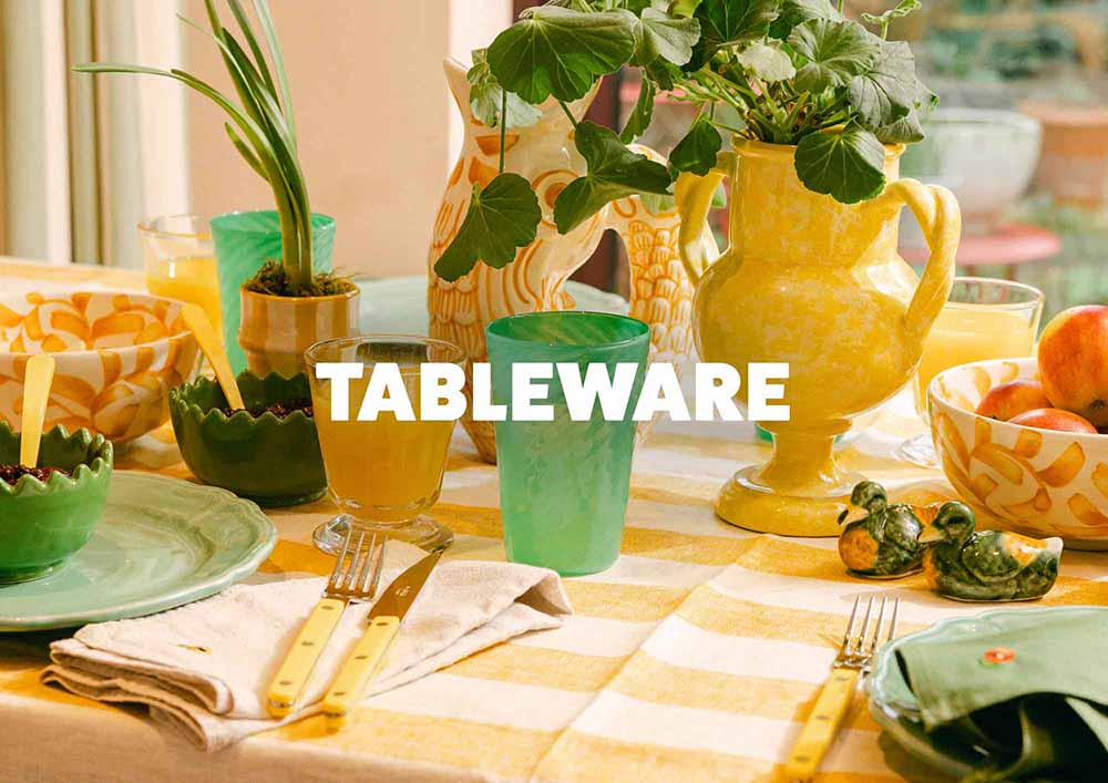 Table setting with tableware including cups, plates, and cutlery on a striped tablecloth, featuring the text 'TABLEWARE'. LAMP LDN LIVING